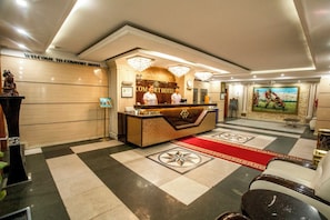 Ein Hotel-Empfangsbereich mit Check-in-Schalter, Rezeption und einem roten Teppich zum Eingangsbereich.