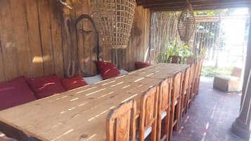 A wooden dining table with chairs, a woven ceiling, and a view of greenery outside.