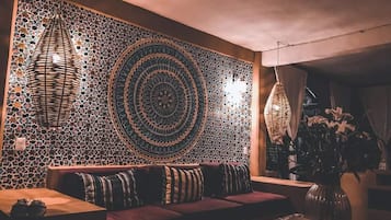 Un coin salon accueillant, avec un mur orné d’un motif, un luminaire en fibres tressées et un vase rempli de fleurs.