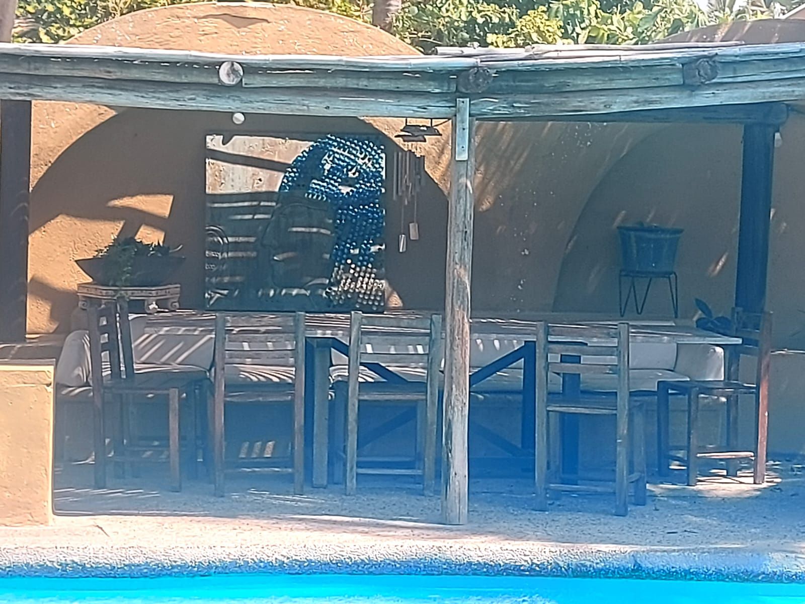 Un espace aménagé au bord de la piscine, comprenant un coin salon couvert, une table et une chaise.