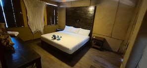 Ein Schlafzimmer mit einem Holzkopfteil, einem Bett mit weißer Bettwäsche, einem Nachttisch und einem Fenster mit Vorhang.