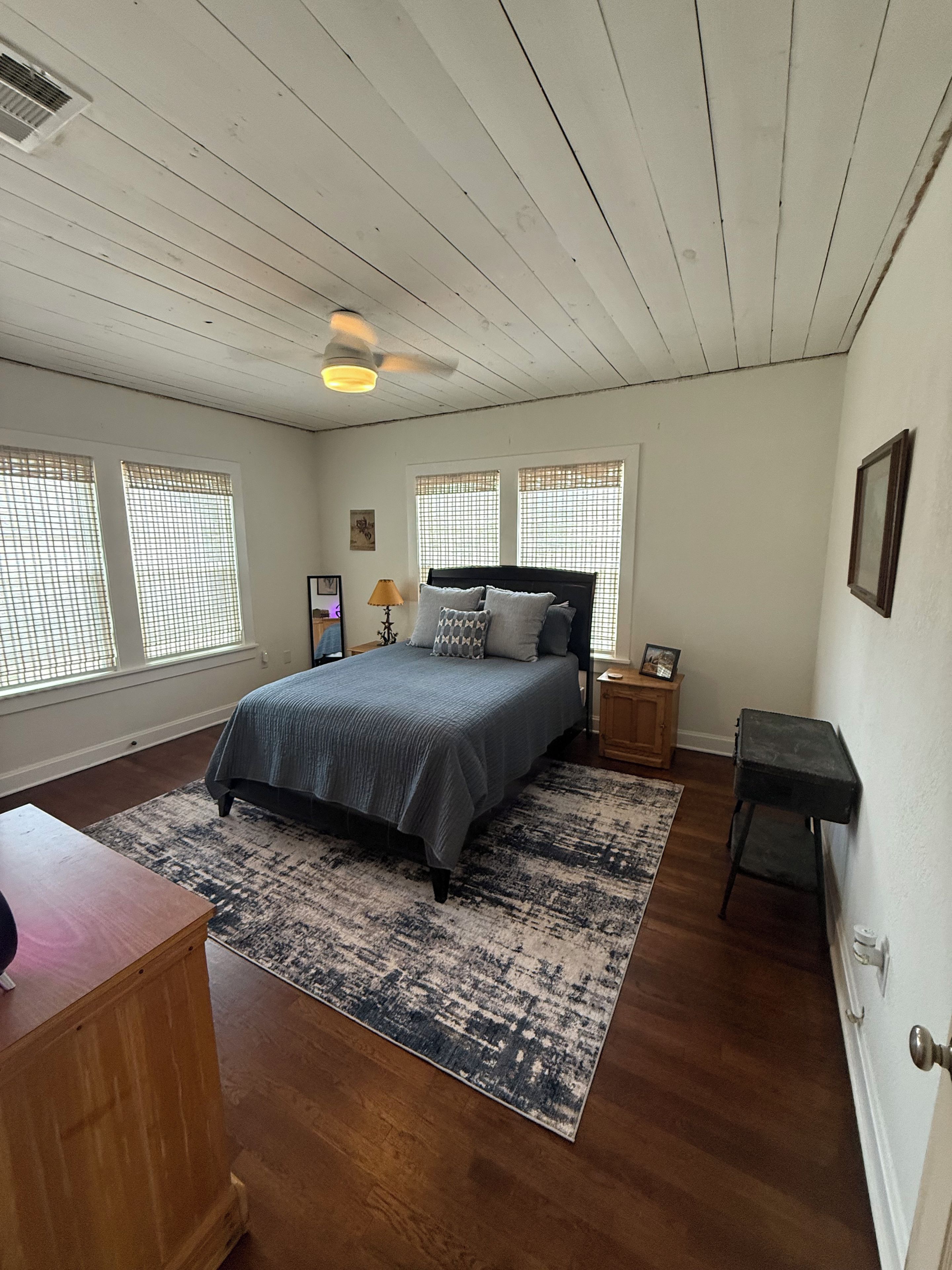 A bedroom with a bed, a desk, a chair, a rug, and a ceiling fan.