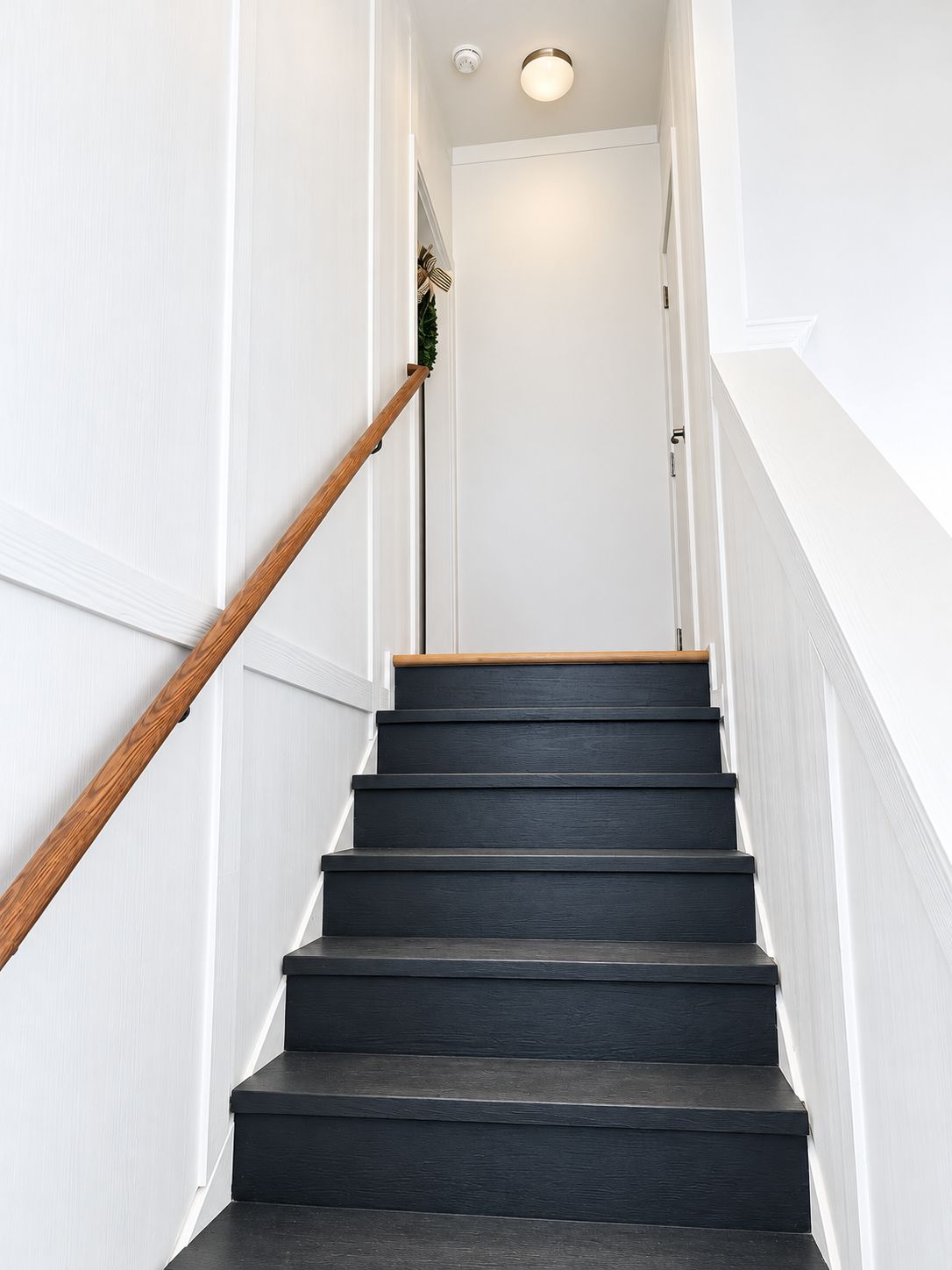 Eine Treppe mit hölzernen Geländern und dunklen Stufen, die zu einer weißen Tür führt.