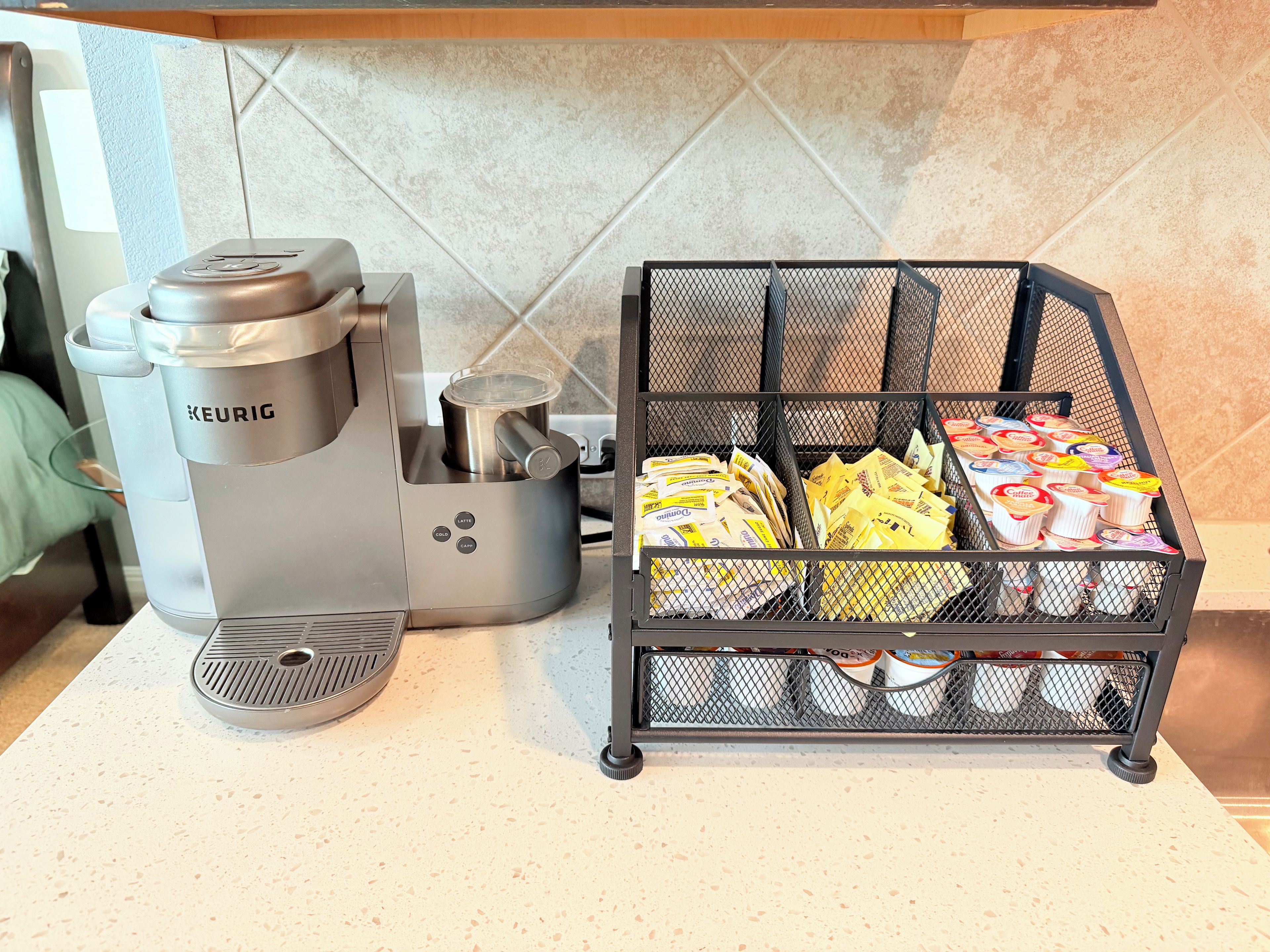 Máquina de café Keurig e um cesto com cápsulas de café em uma bancada de cozinha.
