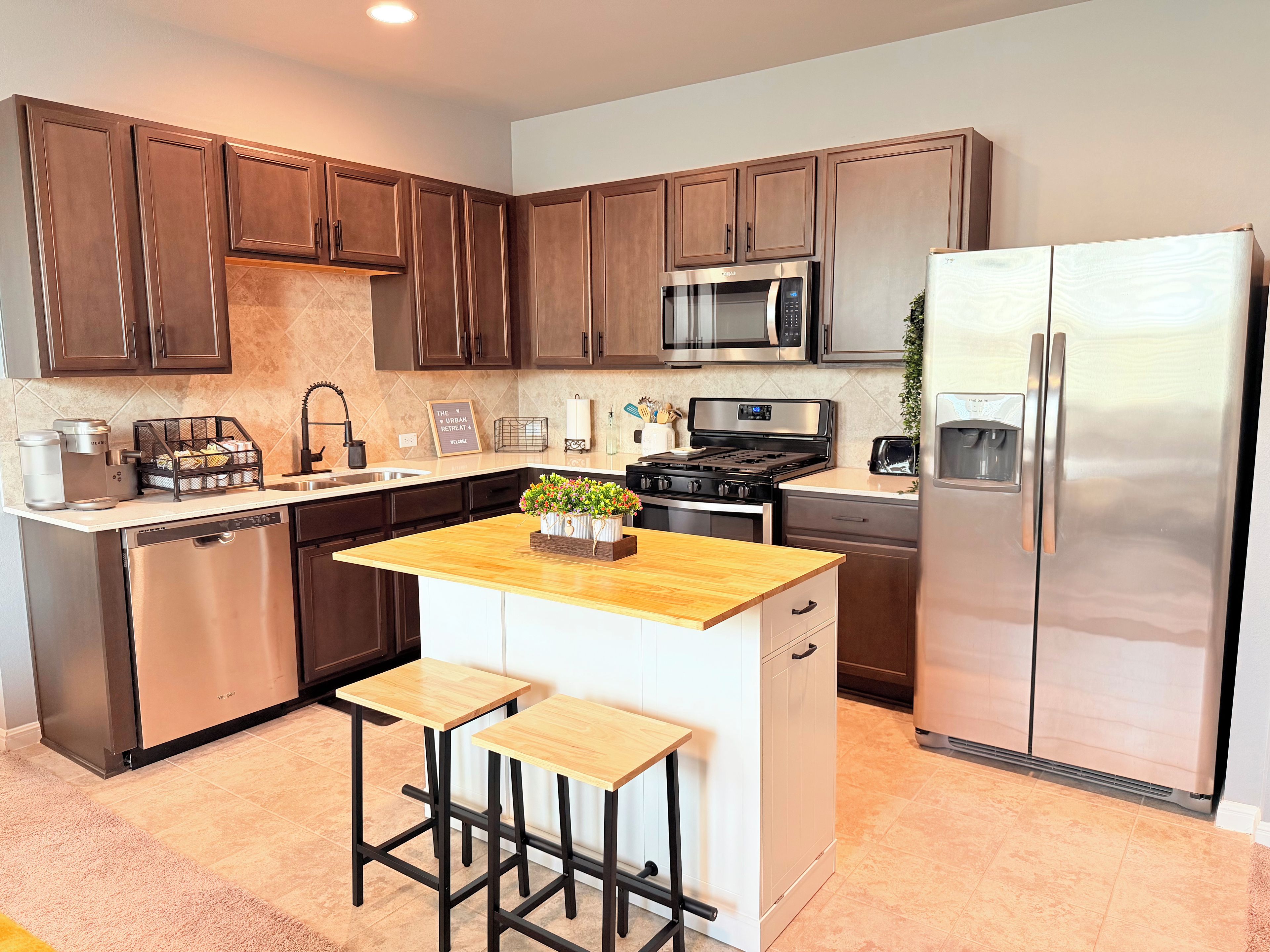 A modern kitchen with stainless steel appliances, wooden cabinets, and a central island with stools.