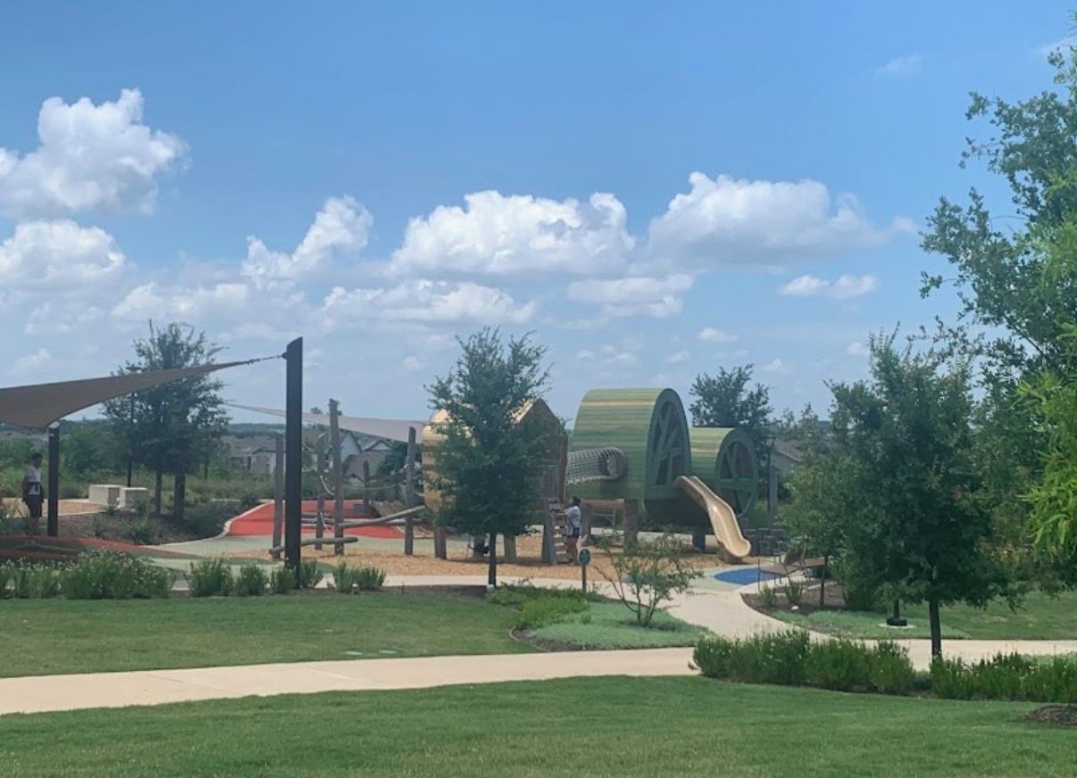 A playground with slides and climbing structures, surrounded by grass and trees.