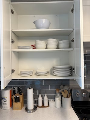 Et køkkenskab med hvide opbevaringshylder, en hvid skål øverst og stakke af hvide tallerkener i de nederste hylder.