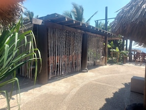 Un espace extérieur aménagé avec des sièges, abrité par un toit de chaume, entouré de plantes tropicales et recouvert de gravier.