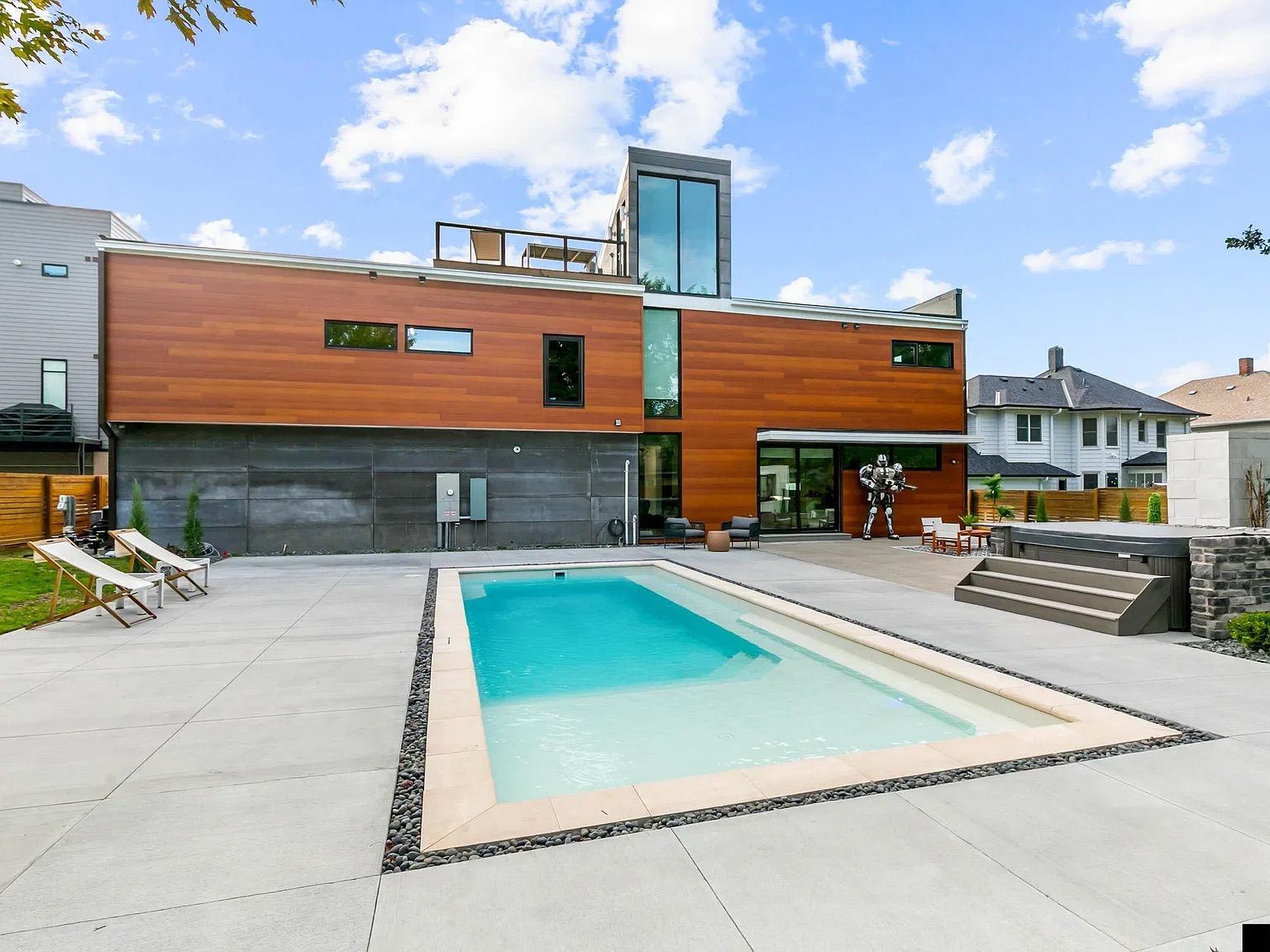 A modern two-story house with a swimming pool, outdoor seating, and a staircase leading to the upper level.