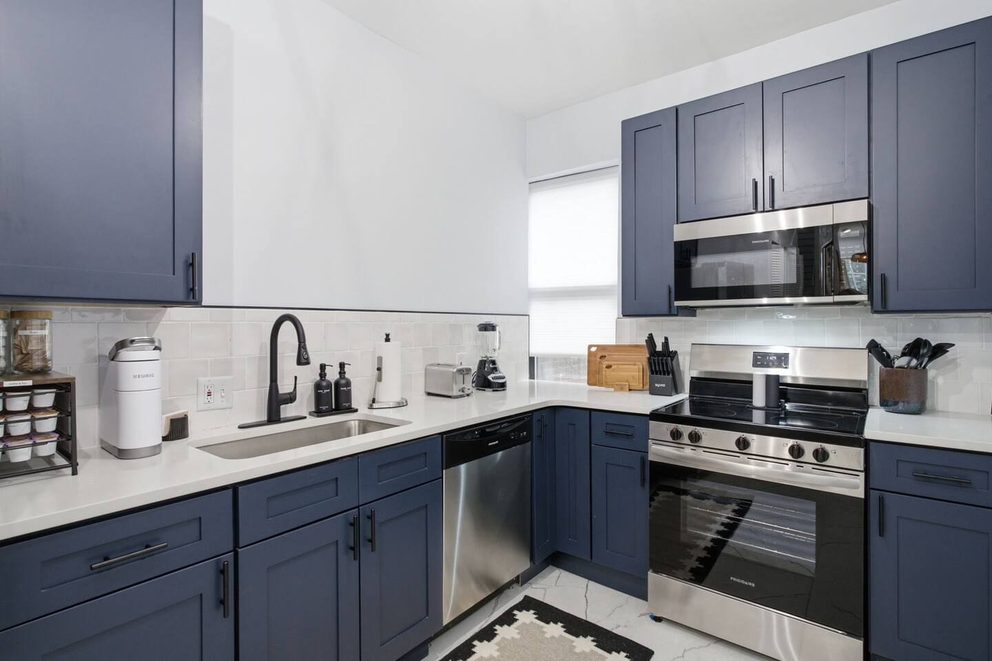 A modern kitchen with dark blue cabinets, a stainless steel range, and a built-in microwave.