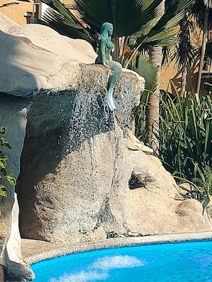 Eine Meerjungfrau Statue sitzt auf einem Felsen an einem Pool.