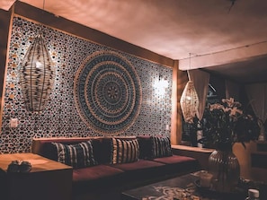 Eine gemütliche Sitzecke mit einer gemusterten Wand, einer gewobenen Leuchte und einer Vase mit Blumen.