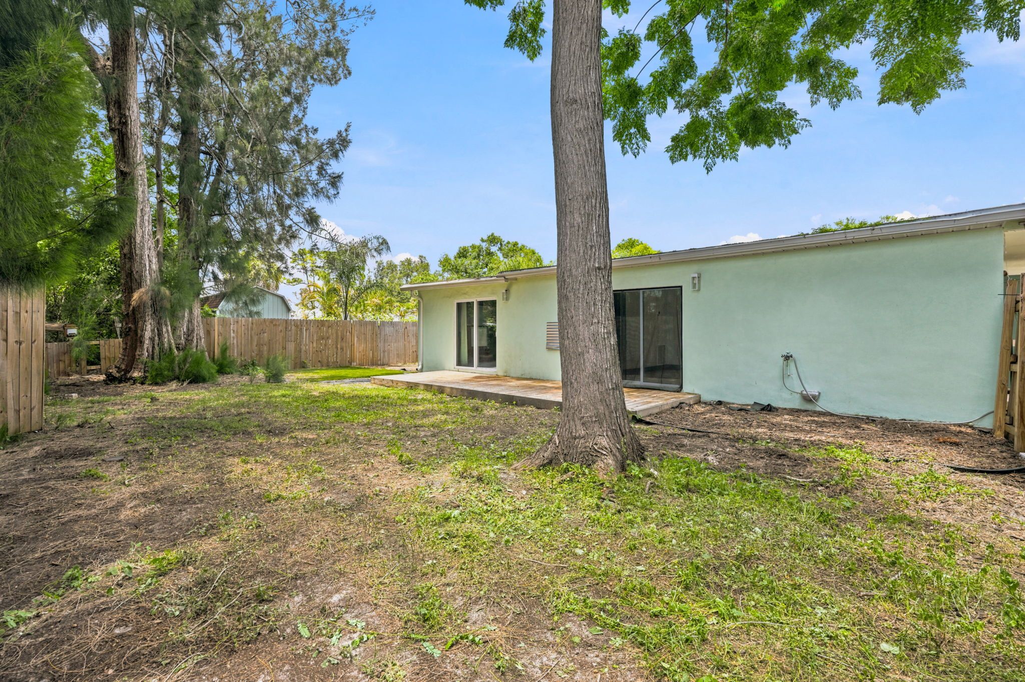 A residential backyard with a single-story house, a wooden fence, and a tree.