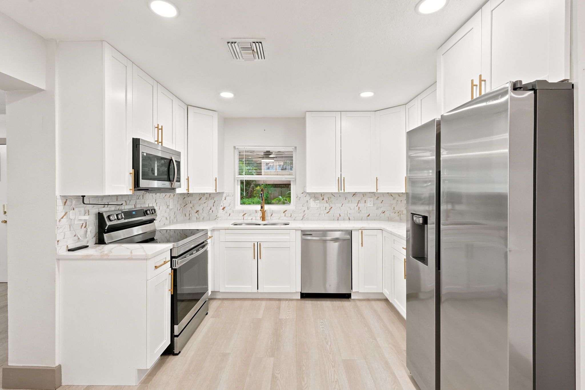 A modern kitchen with white cabinetry, stainless steel appliances, and a wooden floor.