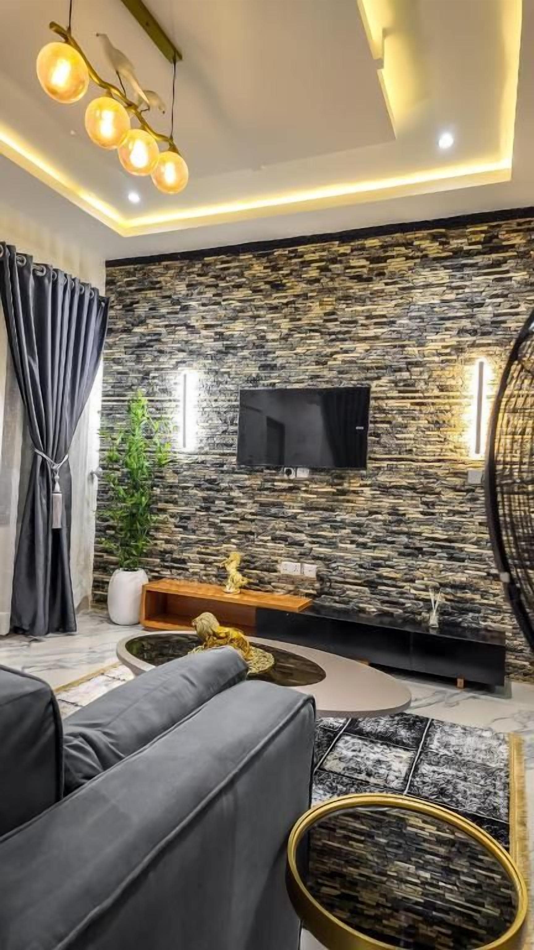 Ein modernes Wohnzimmer mit einer Steinwand, einem Flachbildfernseher, einer Couch, einem Couchtisch und einer Zierpflanze.