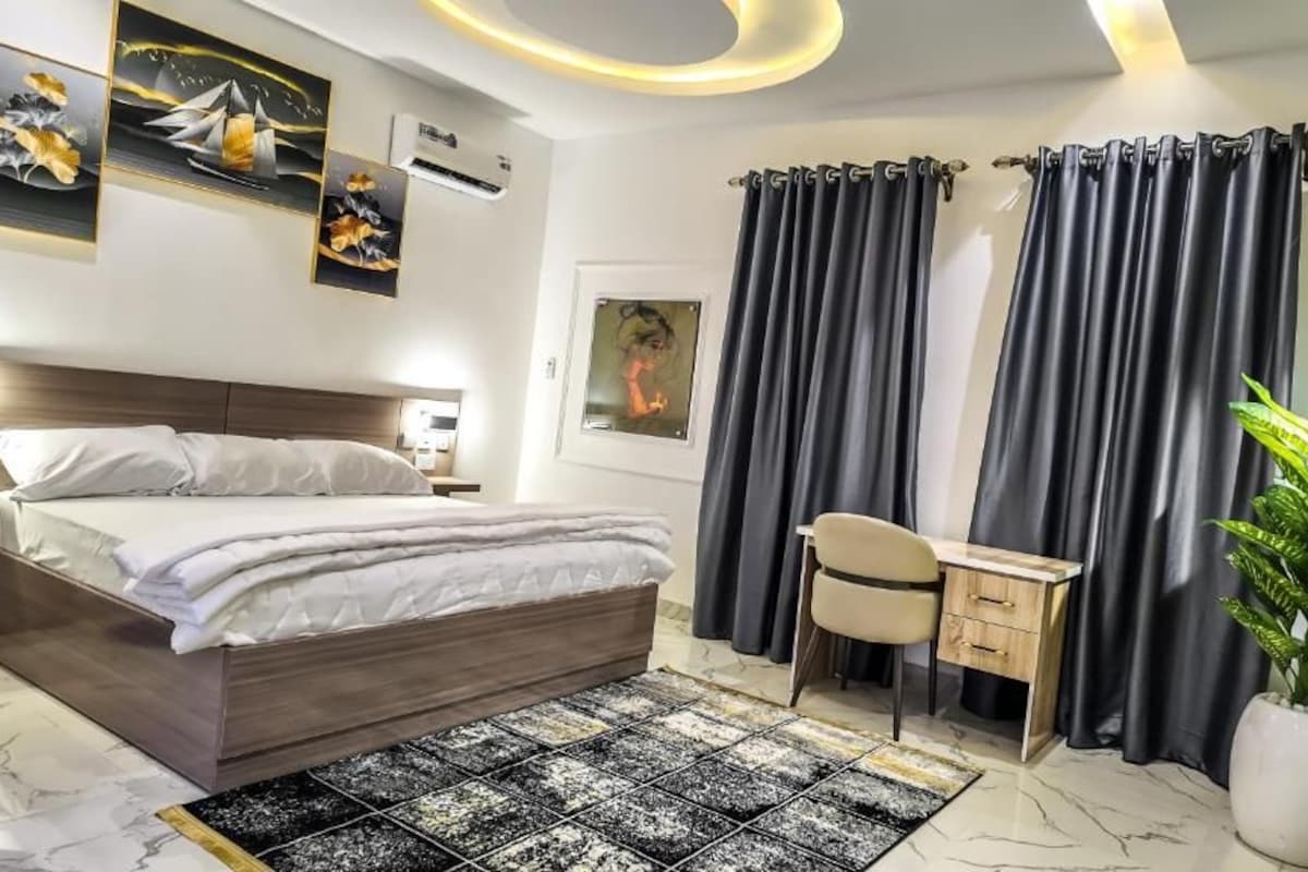 A modern hotel room with a bed, desk, chair, and a potted plant.