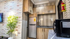 A kitchen with wooden cabinets, a stainless steel refrigerator, a microwave, and a fire extinguisher on the wall. - Jayhaven Crystal Serviced Apartment (Uyo)