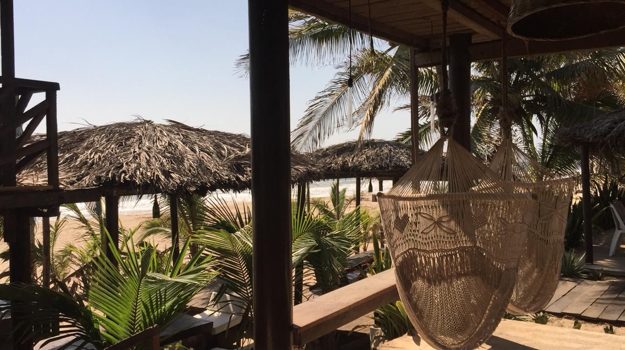 Un espace de détente aménagé sur la plage, avec des parasols en chaume, des meubles en osier et des palmiers.