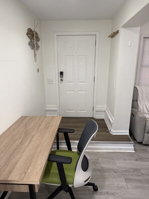Une pièce avec une table en bois, un fauteuil de bureau vert et noir, une porte blanche et un canapé gris.