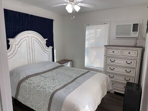 Quarto com cama, cômoda, ventilador de teto e aparelho de ar condicionado.