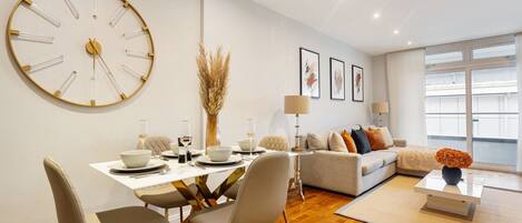 A modern living room with a dining area, featuring a large wall clock, a sofa set, and a coffee table.