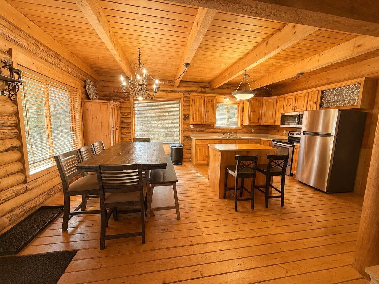A log cabin interior with a dining table, chairs, a kitchen area with a refrigerator, and wooden walls.