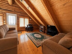 A cozy attic room with wooden beams, a sofa, a TV, and a bookshelf. - Mountain View Hideaway (Brian Head)