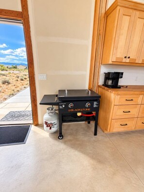 A kitchenette with a Blackstone gas stove, a coffee maker, wooden cabinets, and a propane tank. - Barndo Retreat | Big Spaces + Mountain Views (Cedar City)