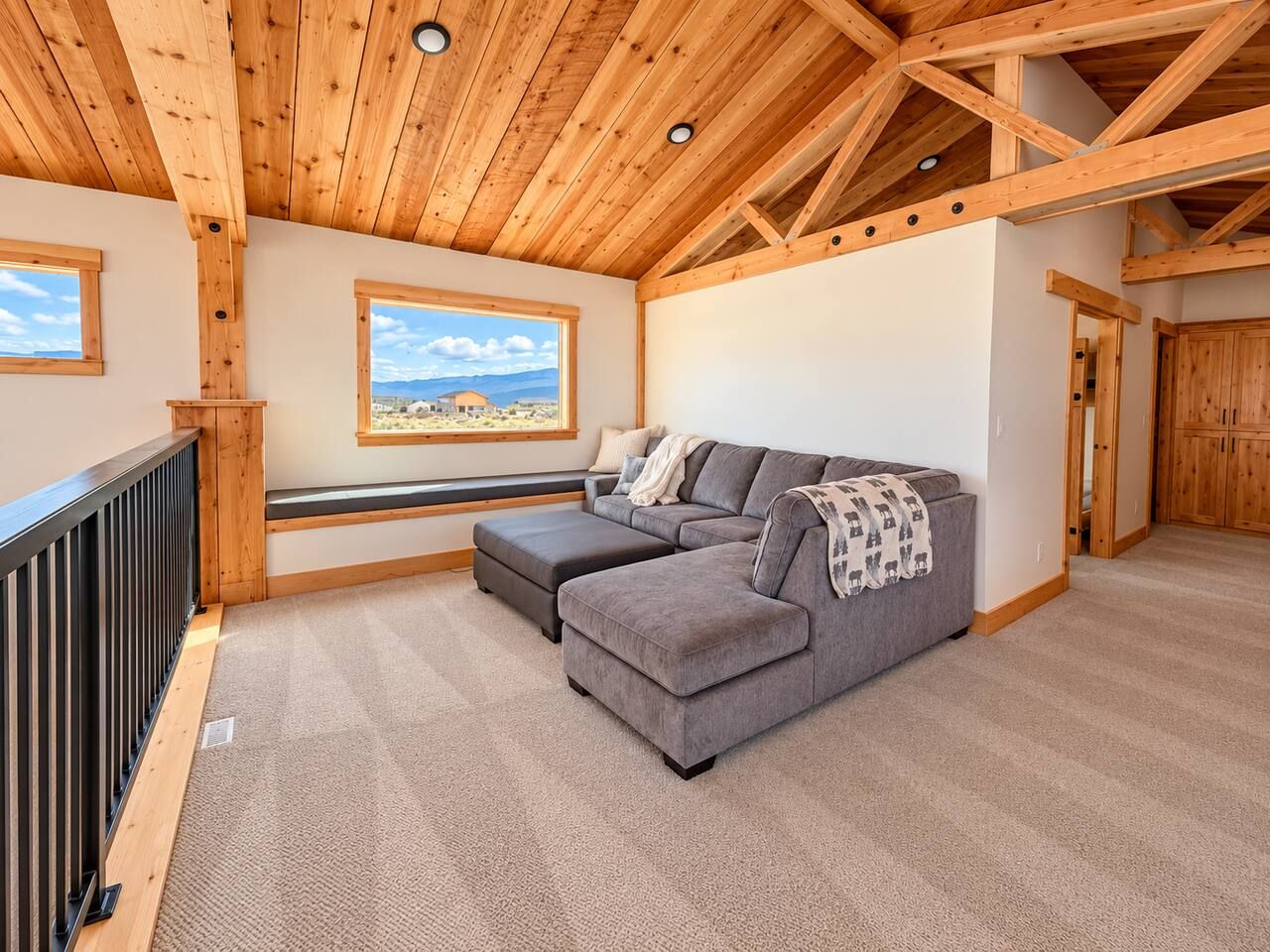A modern living room with a sectional sofa, a window with a view, and a wooden ceiling.