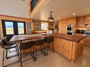 A kitchen with a central island, wooden cabinets, and a large window. - Barndo Retreat | Big Spaces + Mountain Views (Cedar City)