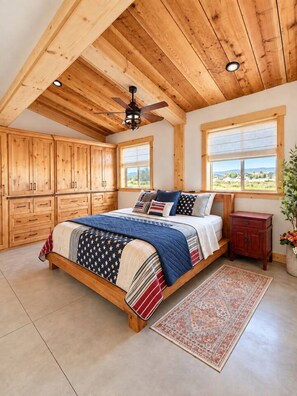 Un dormitorio con techo de madera, una cama con colcha estampada, una mesita de noche y una ventana con vistas.