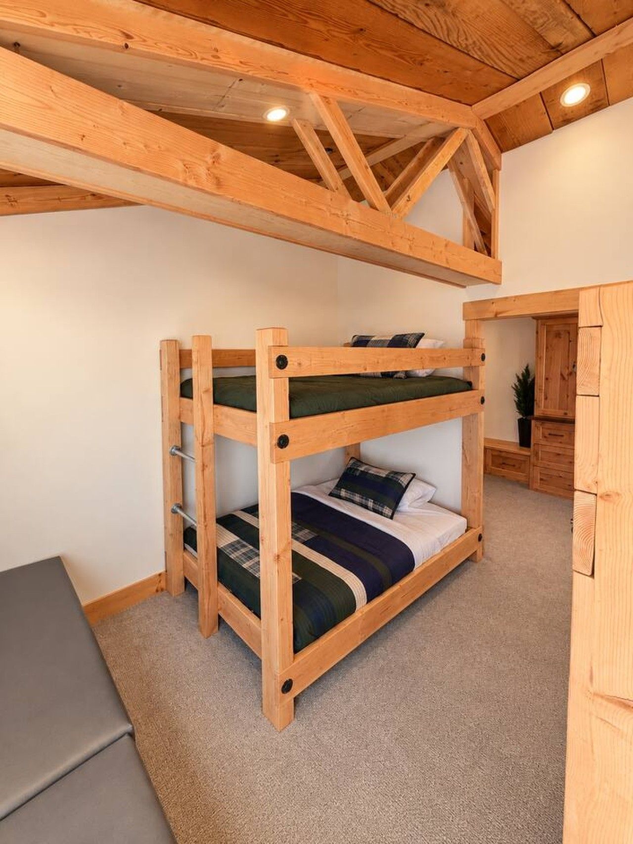 A bunk bed with a wooden frame and a desk in a room with a sloped ceiling and wooden beams.