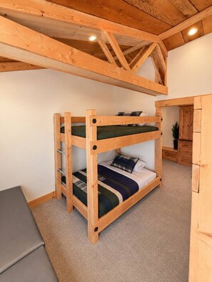 Ein Stockbett mit Holzrahmen und einem Schreibtisch in einem Raum mit schrägen Wänden und Holzbalken.