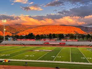 Un estadio de fútbol con un campo extenso, gradas y una montaña al fondo.