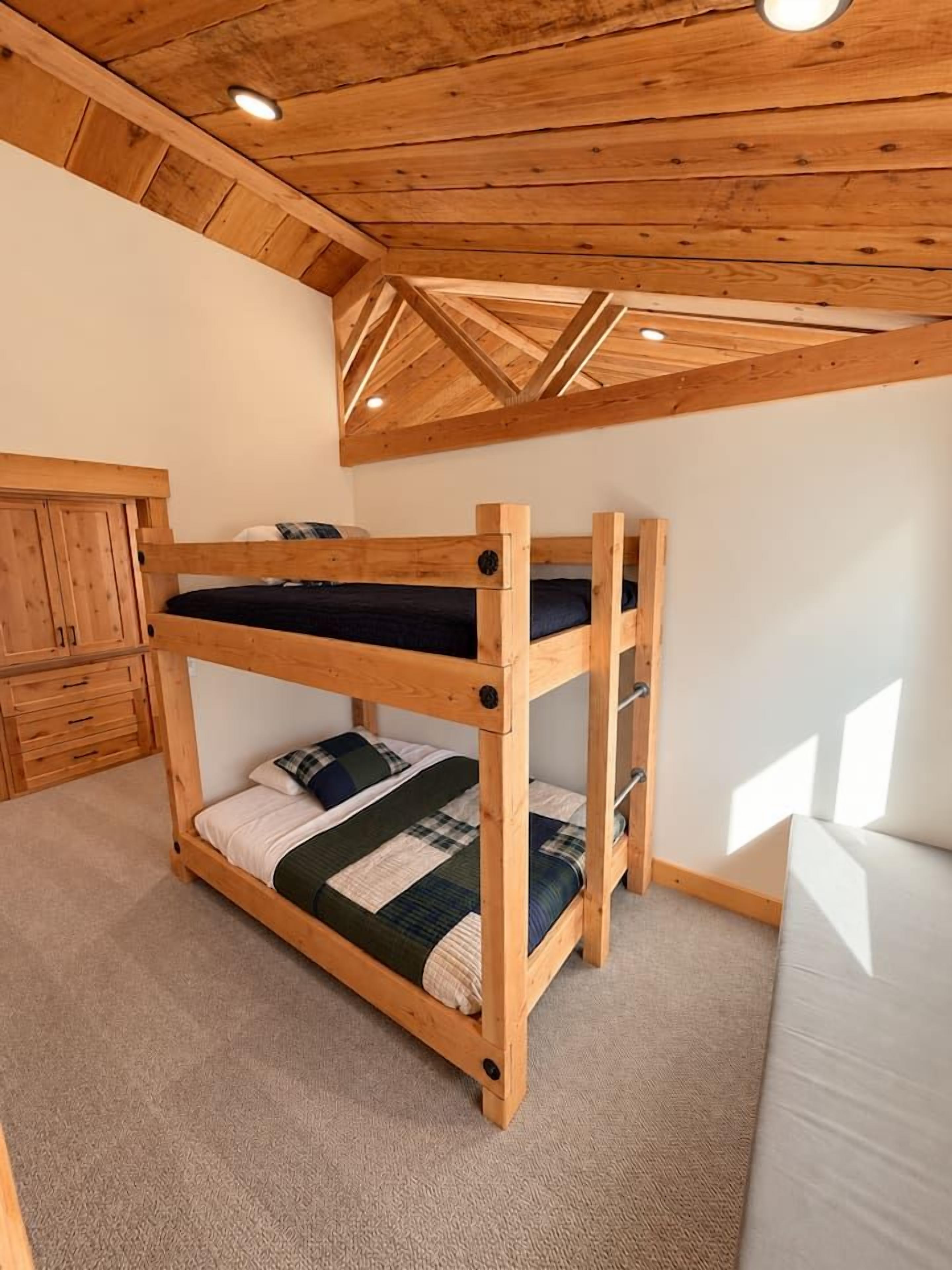 A bunk bed with a wooden frame, a lower bunk with a quilt, and a headboard.