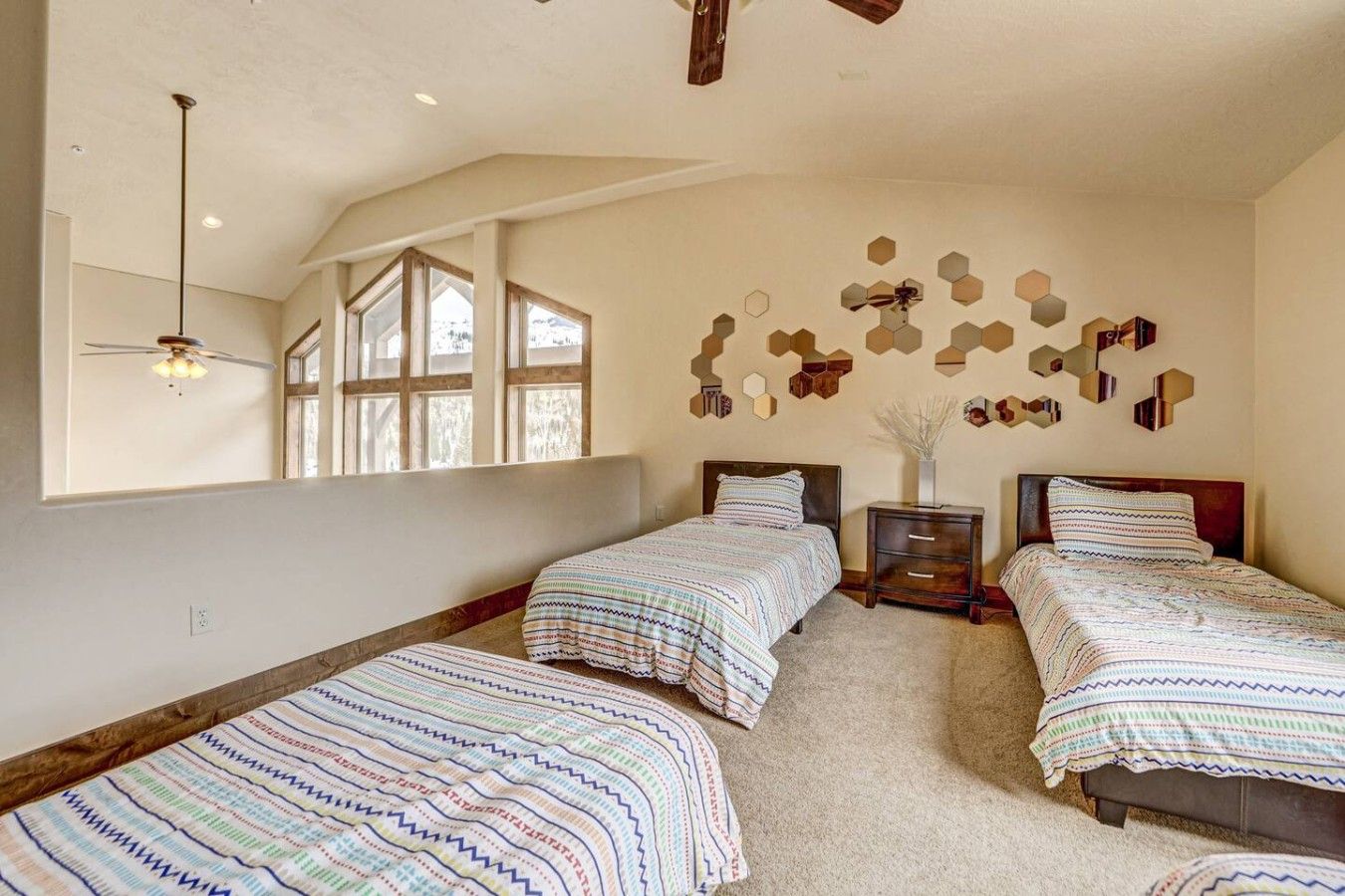 Une chambre avec deux lits, un ventilateur de plafond, une fenêtre et un mur orné de miroirs hexagonaux.