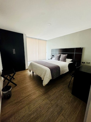 Habitación de hotel con cama, escritorio, armario y ventana con persianas.