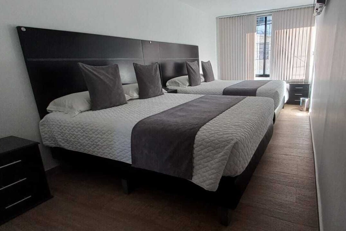 Una habitación de hotel con una cama grande, una mesita de noche, un armario y una ventana con cortinas.