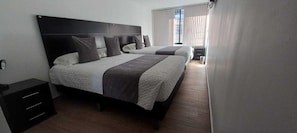 Una habitación de hotel con una cama grande, una mesita de noche, un armario y una ventana con cortinas.