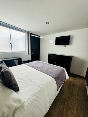 Una habitación de hotel con cama, televisor montado en la pared y escritorio.