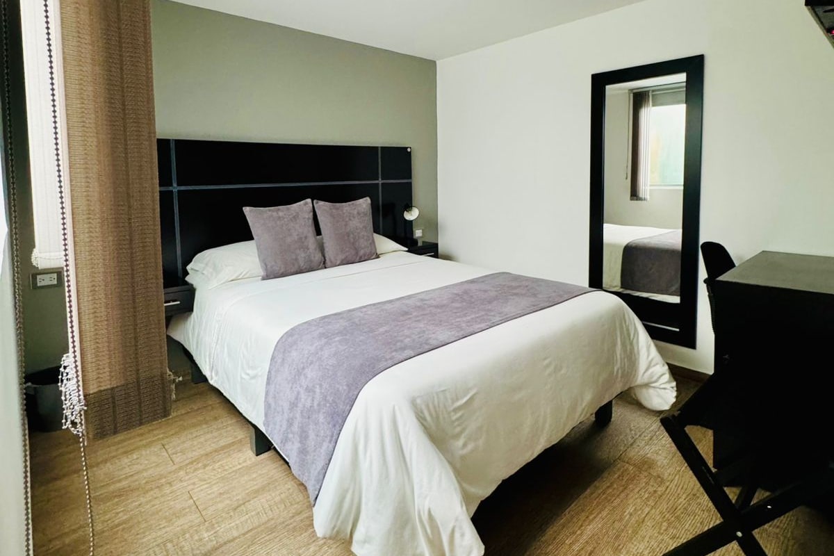 Una habitación de hotel con cama, escritorio y espejo.