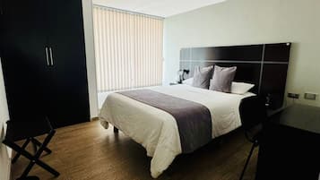 A hotel room with a bed, a desk, a wardrobe, and a window with blinds.