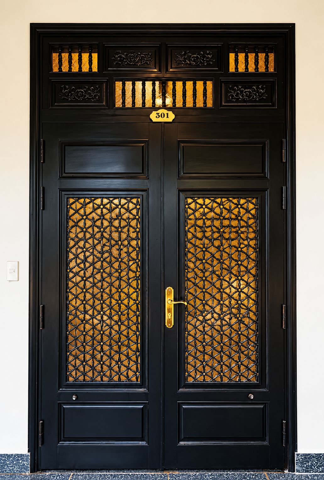 A black double door with a number plate, a patterned glass panel, and a brass handle.
