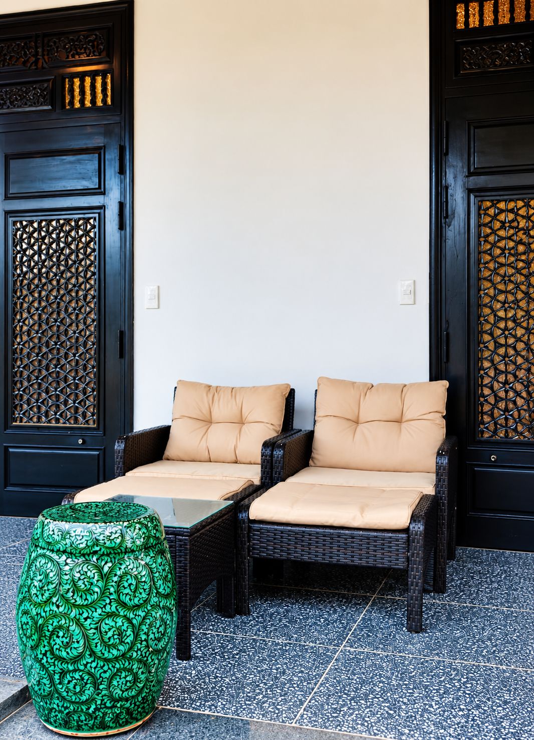 A seating area with two wicker chairs and a green decorative vase.