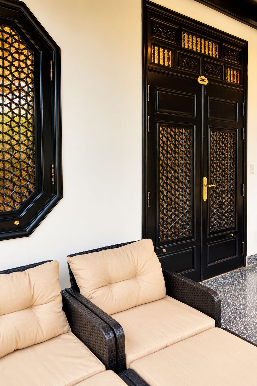 A hotel entrance with two black doors, each with a numbered plaque, and a seating area with beige cushions.
