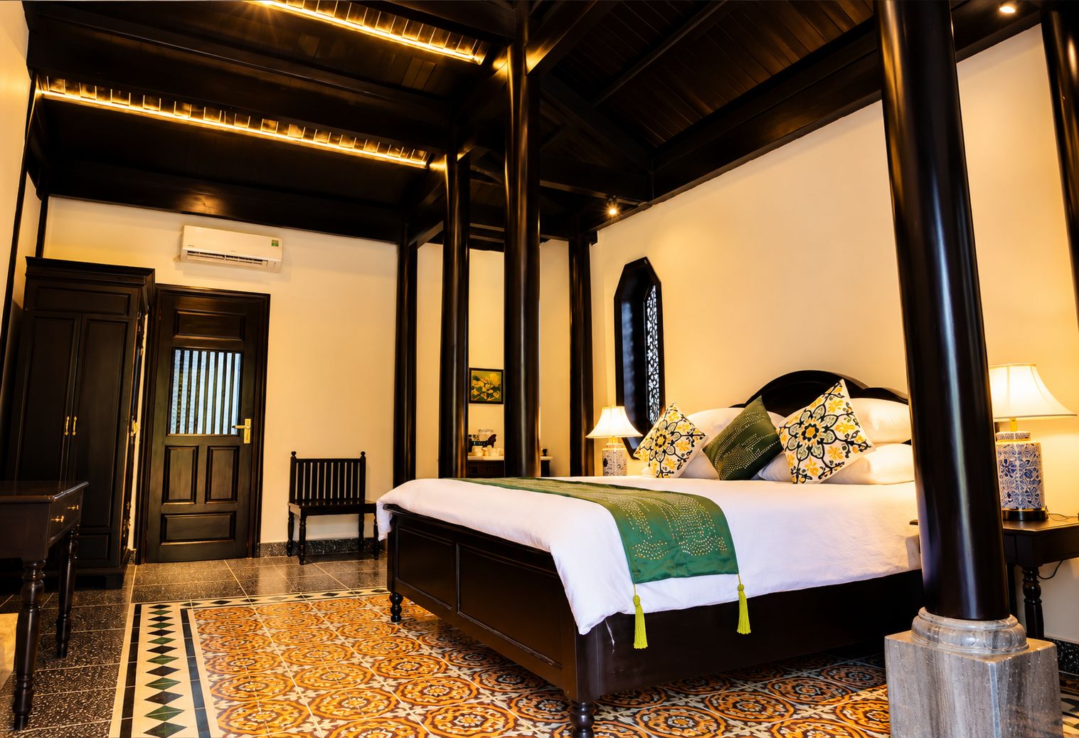 Quarto de hotel com uma cama grande, um banco, uma escrivaninha e piso estampado.