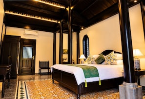 Quarto de hotel com uma cama grande, um banco, uma escrivaninha e piso estampado.