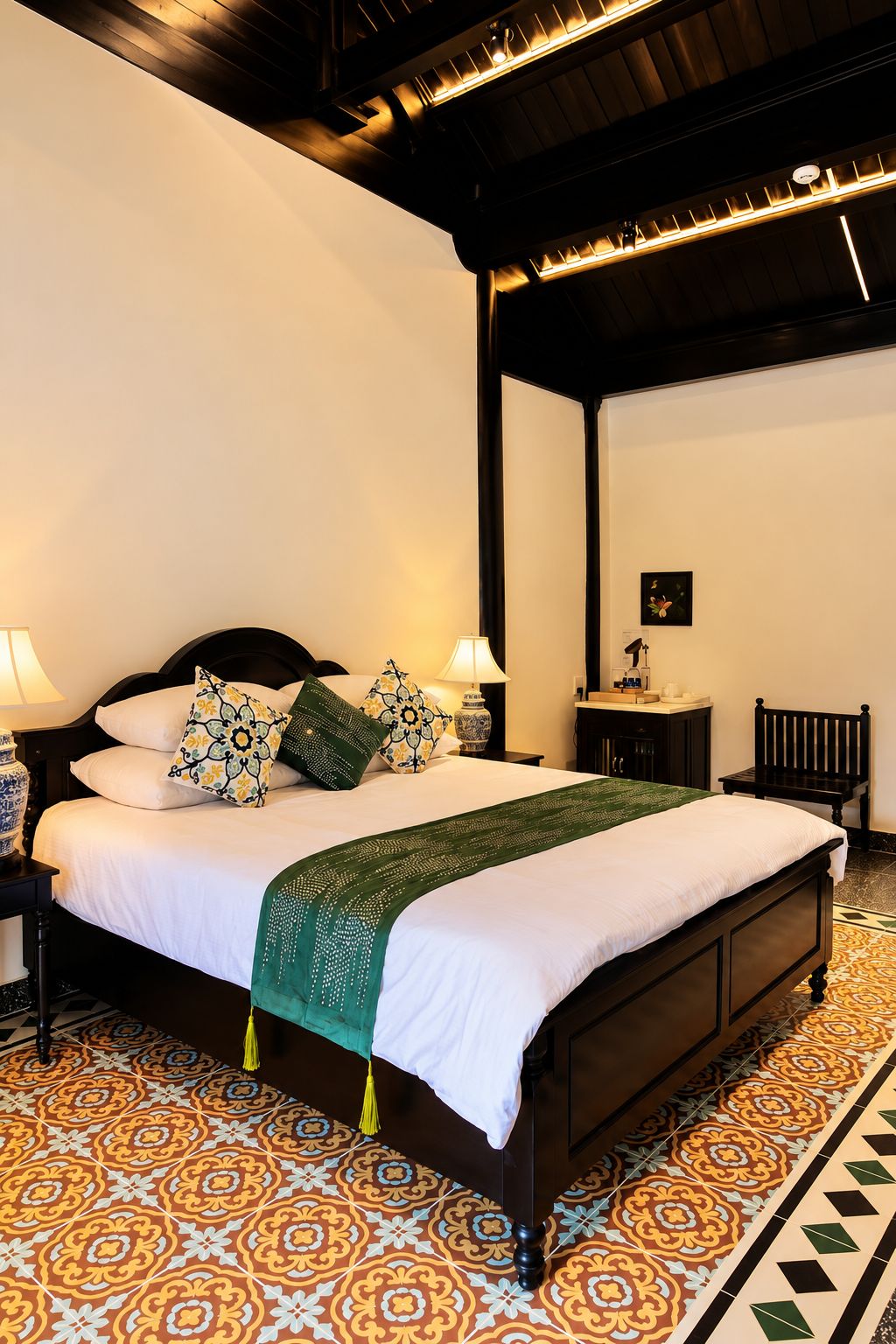 Cama bem arrumada com manta verde, mesa de cabeceira com abajur e cadeira em um quarto com ladrilhos estampados.