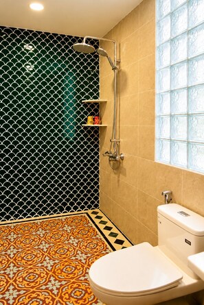 Casa de banho com chuveiro, sanita e pavimento em azulejos estampados.
