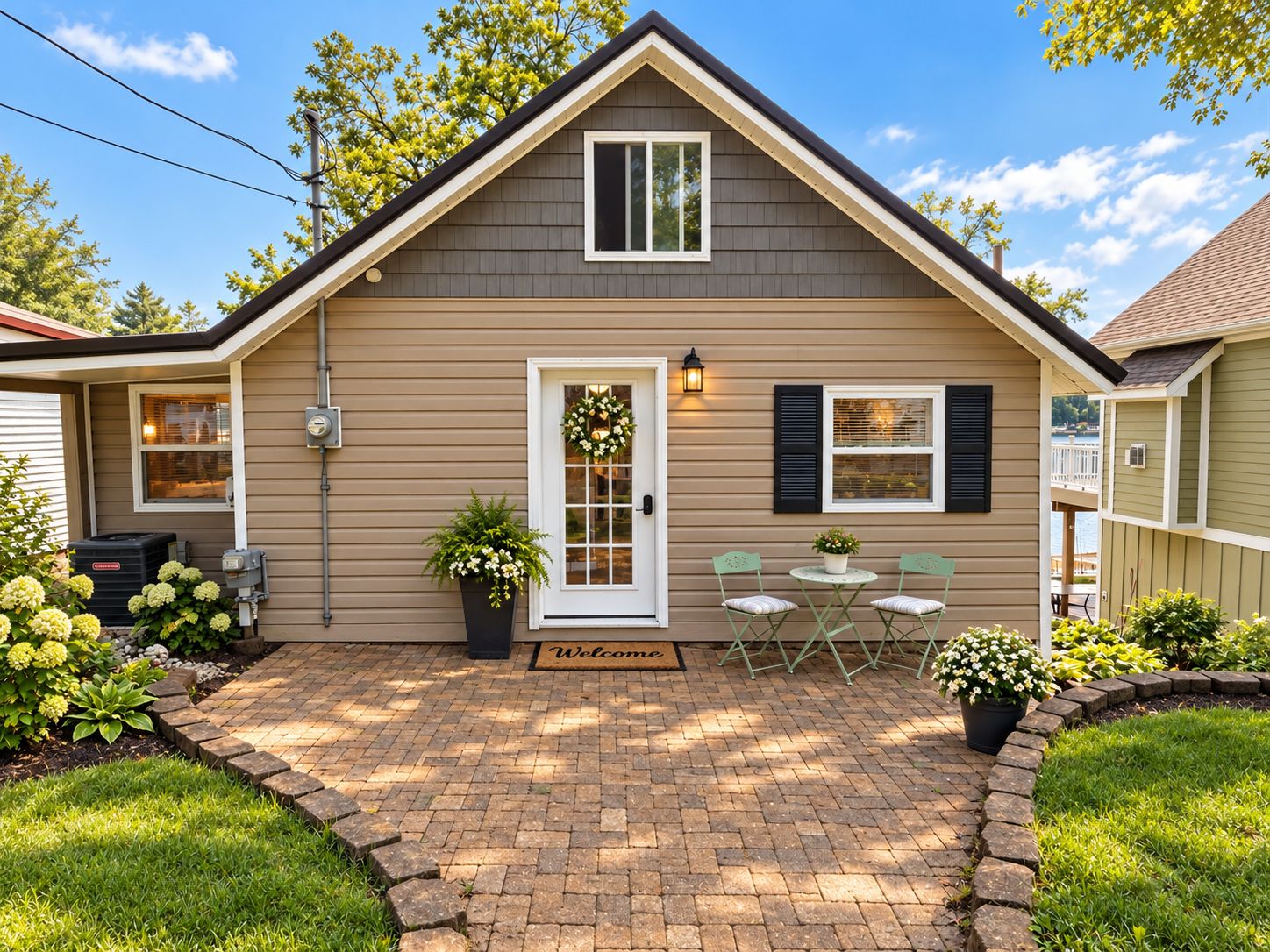 A single-story house with a front porch, a welcome mat, and a small patio area with two chairs.